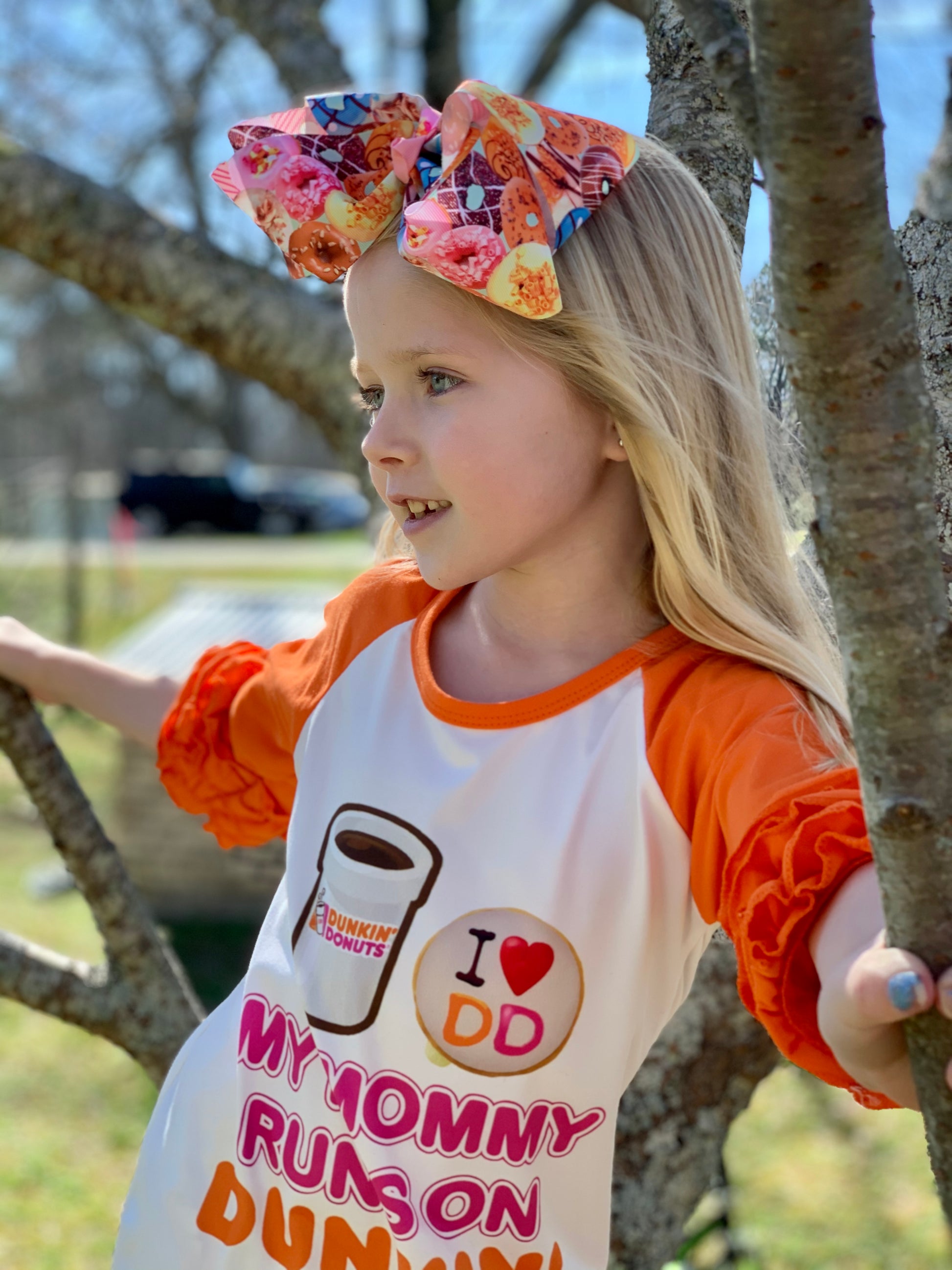 Little girl with blonde hair and a big donut hair bow in a Dunkin Donuts shirt